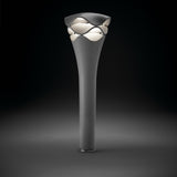 Cornet B/77 tiered LED bollard light in stone grey aluminium, with a slender flared stem rising to a wavy layered head glowing warm white, shown on a dark background.