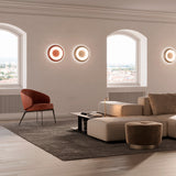 Superbold LED Wall & Ceiling Light 44.3cm, round flush fittings with warm white glowing rings, shown on a living room wall above a sofa and armchair.