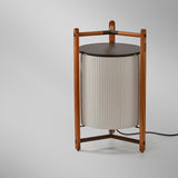 Kando P/76 Ribbon LED floor lamp with cream pleated cylinder shade in a teak wood tripod frame and round brown top, shown on a plain light background.