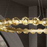 Murané R 18 ring chandelier close-up showing caramel glass spheres with rippled texture above and below a slim brushed champagne ring, integrated LED, against a grey interior backdrop.