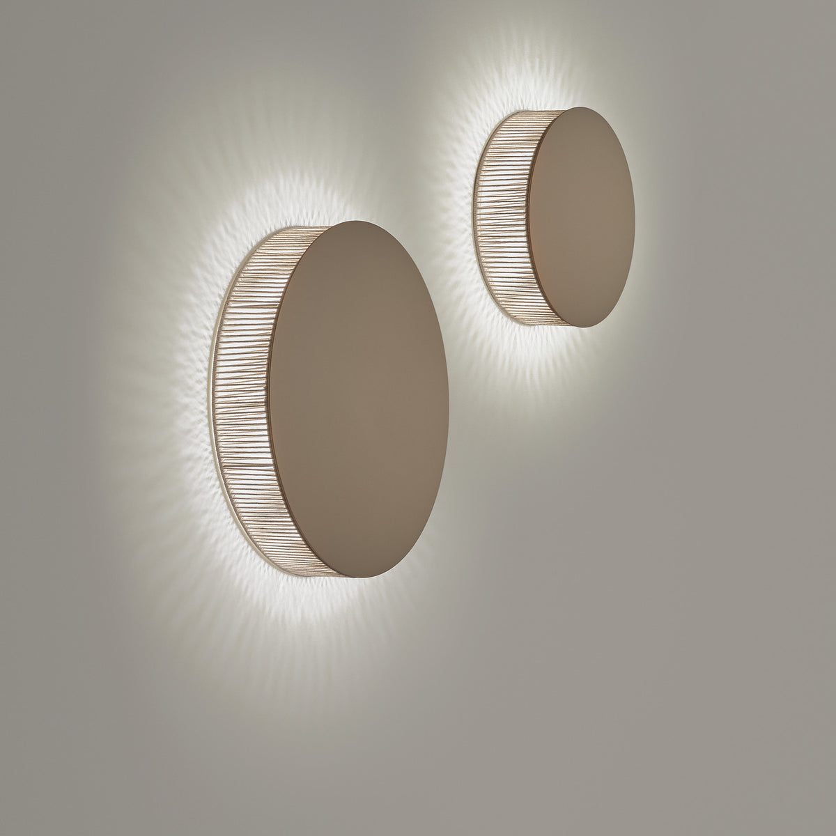 Helios A/01 round LED wall lights with solid brown disc fronts and beige cotton thread edges, casting a soft radial glow on a plain grey wall.