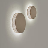 Helios A/01 round LED wall lights with solid brown disc fronts and beige cotton thread edges, casting a soft radial glow on a plain grey wall.