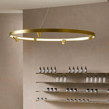 Arena Aluminium Ring LED Pendant Light 147cm in brushed brass, a slim circular hoop with integrated warm white LED and small spotlight heads, shown suspended above open shelving.
