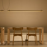 Solid SH Sens 160 cylinder LED pendant light in black, a slim horizontal tube suspended above a wooden dining table and chairs, casting warm ambient light.