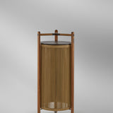 Kando P/111/R rechargeable outdoor floor lamp with sand nautical cord cylinder, teak wood frame, brown top disc, and three-legged base on a light grey background.
