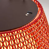 Close-up of the Nans Bag/38/R rechargeable outdoor floor lamp, showing its red woven lattice shade and dark flat top with a recessed handle, illuminated from within.