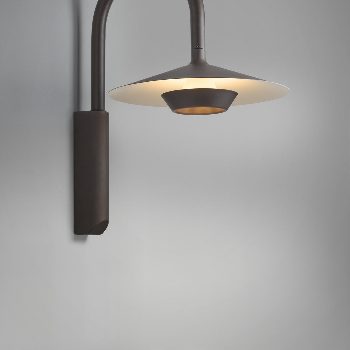 Fanalet A/02 outdoor wall light with a tall arched arm in graphite brown and a wide flat shade with white underside, illuminated against a plain grey background.