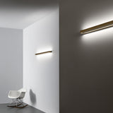 Zero Line Metal Linear LED Wall Light, 52cm brass bar fixture shown on a grey and white wall in a room with a white rocking chair, casting warm linear light.