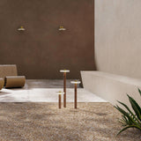 Venexia Glass LED Outdoor Floor Lamp in three heights, slim wood columns with round matt brass bases and glass discs, set on gravel in a courtyard.