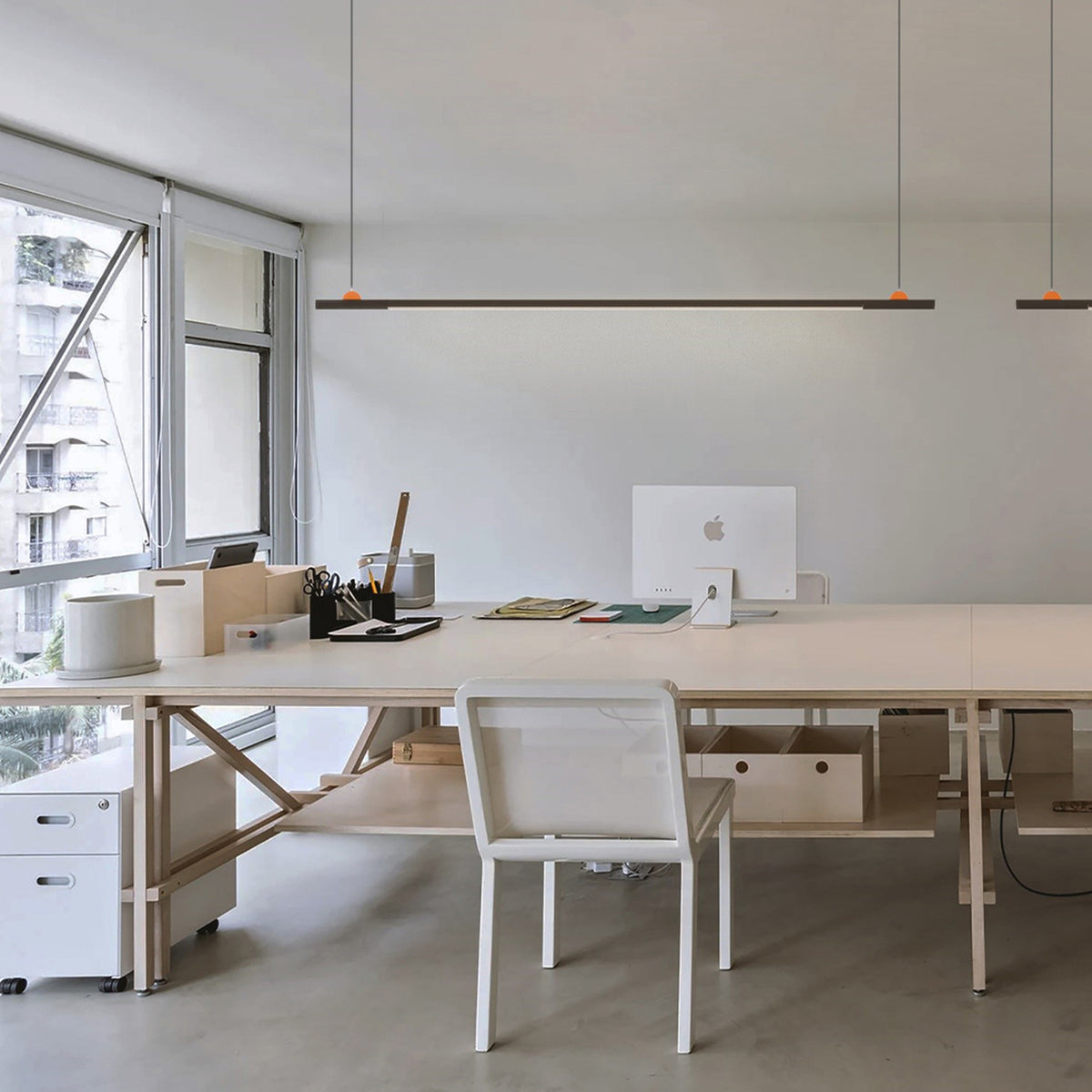 BIMU S100 Ele linear LED pendant light in black, slim bar suspended on two thin cables above an office desk with chair and computer monitor.