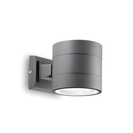 Introducing the Opus Round Outdoor Wall Light - Anthracite: a sleek, cylindrical fixture with a matte anthracite finish, designed for outdoor use. It features a downlight orientation and is crafted with durable Pyrex glass, mounted on a rectangular base secured with screws.