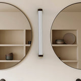 Roseline LED Ribbed Glass Linear Wall Light in gold and brown, mounted vertically between two round mirrors above display shelving with bowls and plates.