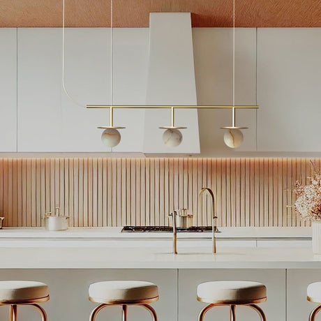 Royal Linear 3 Light Alabaster Chandelier in Gold & Polished Brass, three round globes under brass discs on a slim bar, shown above a kitchen island.