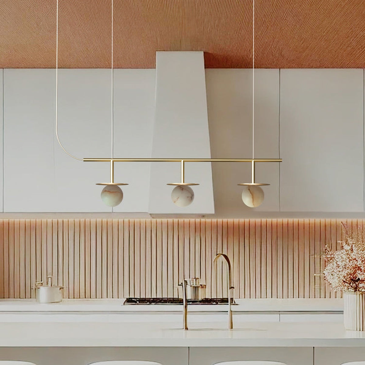 Royal Linear 3 Light Alabaster Chandelier in Gold & Polished Brass, three round globes on brass discs along a slim bar, shown above a kitchen island.