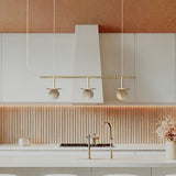 Royal Linear 3 Light Alabaster Chandelier in Gold & Polished Brass, three round globes on brass discs along a slim bar, shown above a kitchen island.