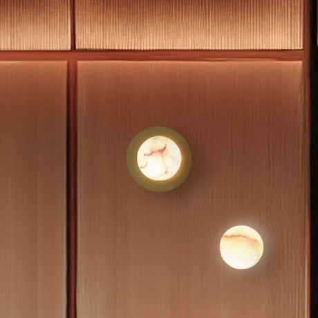Royal wall light with a glowing alabaster globe set against a round brass disc, matt polished brass finish, mounted on a wood-panelled wall.