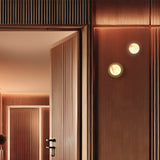 Royal Alabaster Globe Wall Light with Disc in matt polished brass, two fixtures lit on a wood-panelled wall beside a hallway doorway.