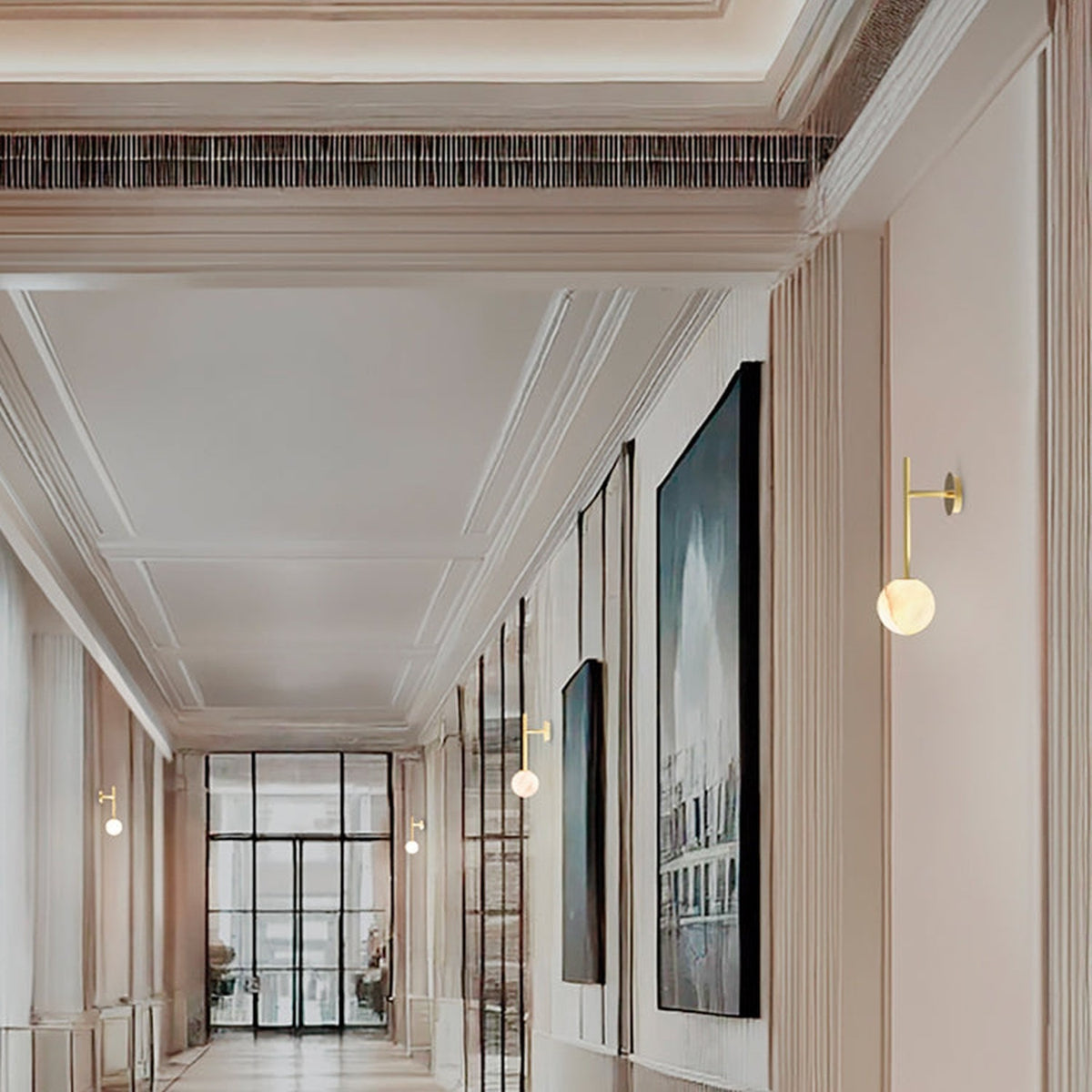 Royal Single Arm Alabaster Globe Wall Light in gold, shown mounted along a hotel corridor wall beside framed artwork, with its round alabaster shade illuminated.