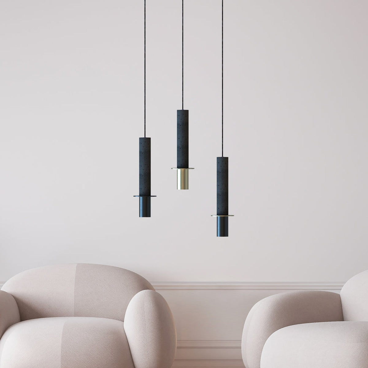 Three Rita concrete pendant lights in charcoal grey with matt black discs and brass or black iron heads, hung at varying lengths above armchairs in a neutral living room.