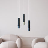 Three Rita concrete pendant lights in charcoal grey with matt black discs and brass or black iron heads, hung at varying lengths above armchairs in a neutral living room.