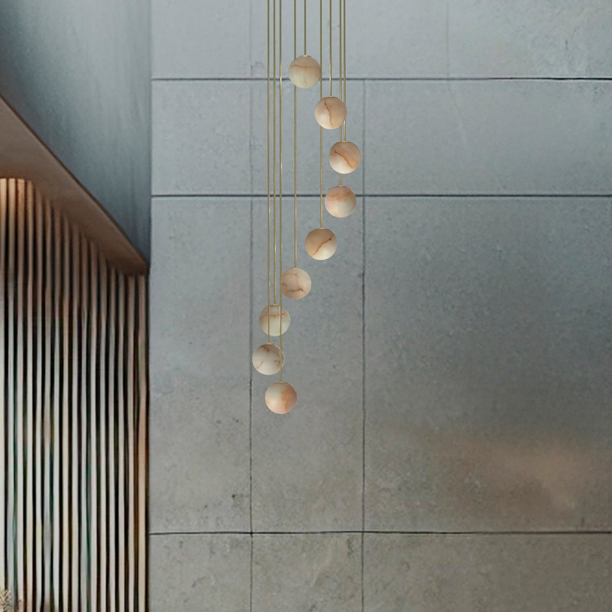 Royal Spiral chandelier with nine alabaster globes cascading on gold cables from a brass ceiling disc, shown against a grey wall.