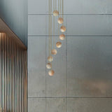 Royal Spiral chandelier with nine alabaster globes cascading on gold cables from a brass ceiling disc, shown against a grey wall.