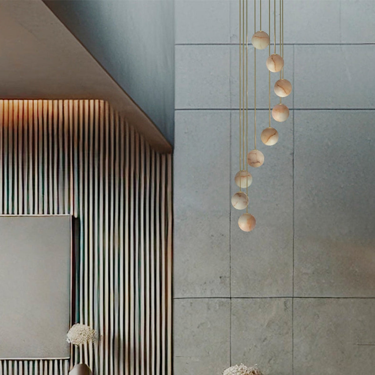 Royal Spiral chandelier with nine alabaster globes cascading on gold cables from a ceiling disc, shown against a stone-tiled wall.