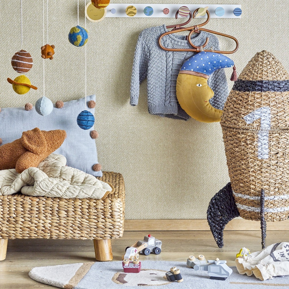Cosmina Rocket Seagrass Basket with Lid in natural woven seagrass, shaped like a rocket with a black fin, displayed in a nursery beside toys and a wall mobile.