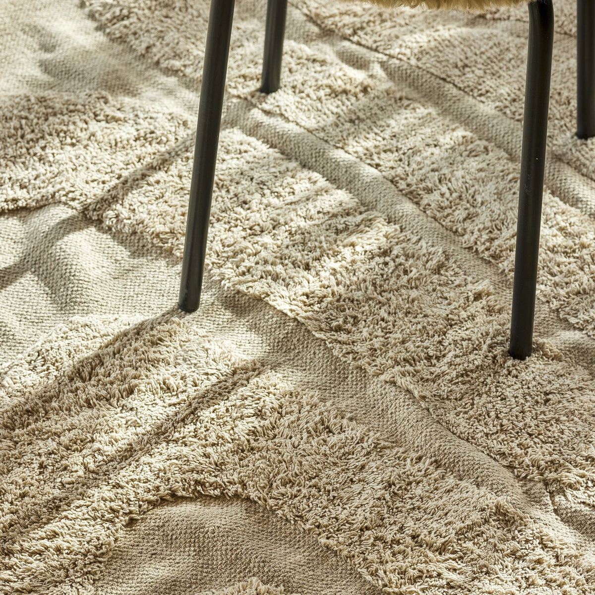 Elaine Wavy Cotton Rug in natural, 210x150cm, flatwoven with raised textured wave lines, shown underfoot beneath dark metal chair legs.