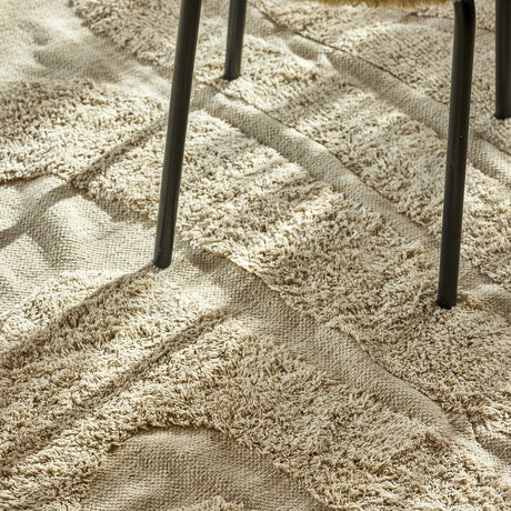 Elaine Wavy Cotton Rug in natural, 210x150cm, flatwoven with raised textured wave lines, shown underfoot beneath dark metal chair legs.