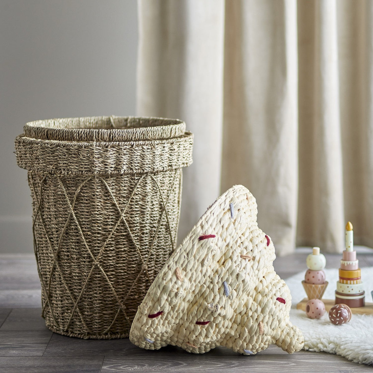Cillie Seagrass Basket with Lid 72cm in Natural, cone-shaped woven body with criss-cross detail and ice-cream swirl lid with stitched accents, shown with toys on a nursery floor.