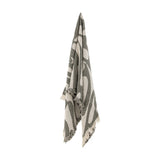 Alk Cotton Throw in green, woven with a large rounded leaf-like pattern and fringed edges, hanging against a plain white background.