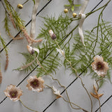 Poppy Artificial Stem in beige with ruffled open flower heads and closed buds on twisting stems, styled with fern fronds and ribbon on a light wood-slat surface.