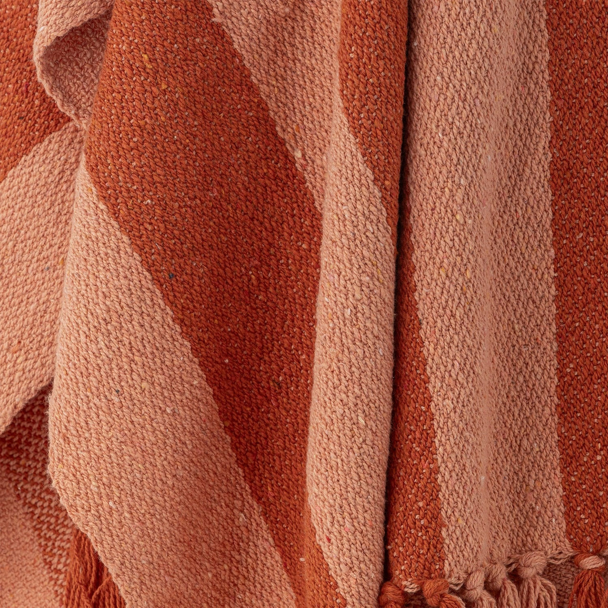 Frello Striped Cotton Throw in Orange, close-up of woven fabric showing broad stripes in two shades of orange with a knotted fringe edge.