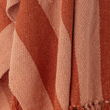 Frello Striped Cotton Throw in Orange, close-up of woven fabric showing broad stripes in two shades of orange with a knotted fringe edge.