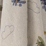 Plane Cotton Throw in beige, close-up of folded cotton fabric showing outlined cloud motifs and a glimpse of a biplane print.