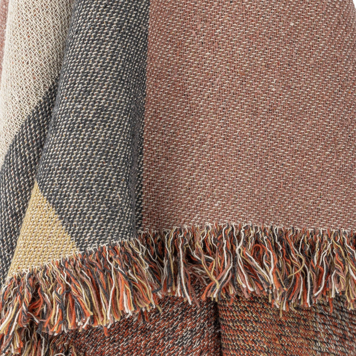 Close-up of the Arni Throw in Multi, showing woven colour-block panels in rust, grey, cream and gold with a thick mixed-yarn fringe edge.