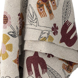 Vivielle Floral Throw in multicoloured fabric, draped in folds showing a textured weave printed with birds, flowers and line-drawn leaves.