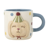 Stoneware kids' mug from the Party Dotted dinner set, cream with multicoloured polka dots, blue handle and interior, and a raised dog face wearing a striped party hat, on a white background.