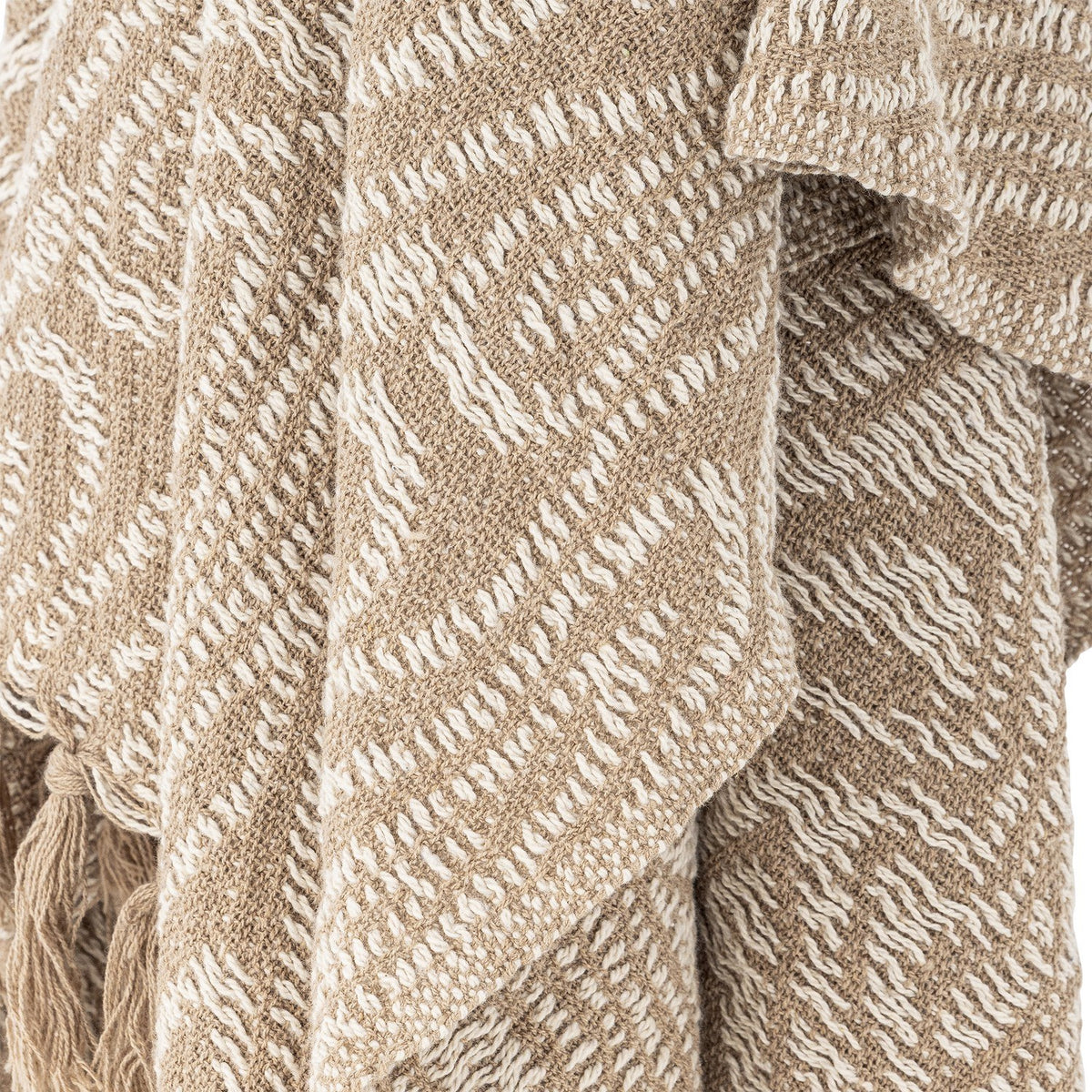 Okapi Cotton Throw in beige, draped in folds showing a woven wavy-line pattern in two tones with fringed tassel edge detail.