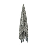 Ugento Leaf Cotton Throw in green, a woven blanket with a tall overlapping leaf pattern and knotted fringe ends, hanging against a plain white background.