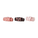 Set of three wrapped-sweet ceramic candle holders in pink, black, and pale pink with hand-painted rings, swirls, and dots, each with a twisted end and taper candle socket, on a white background.
