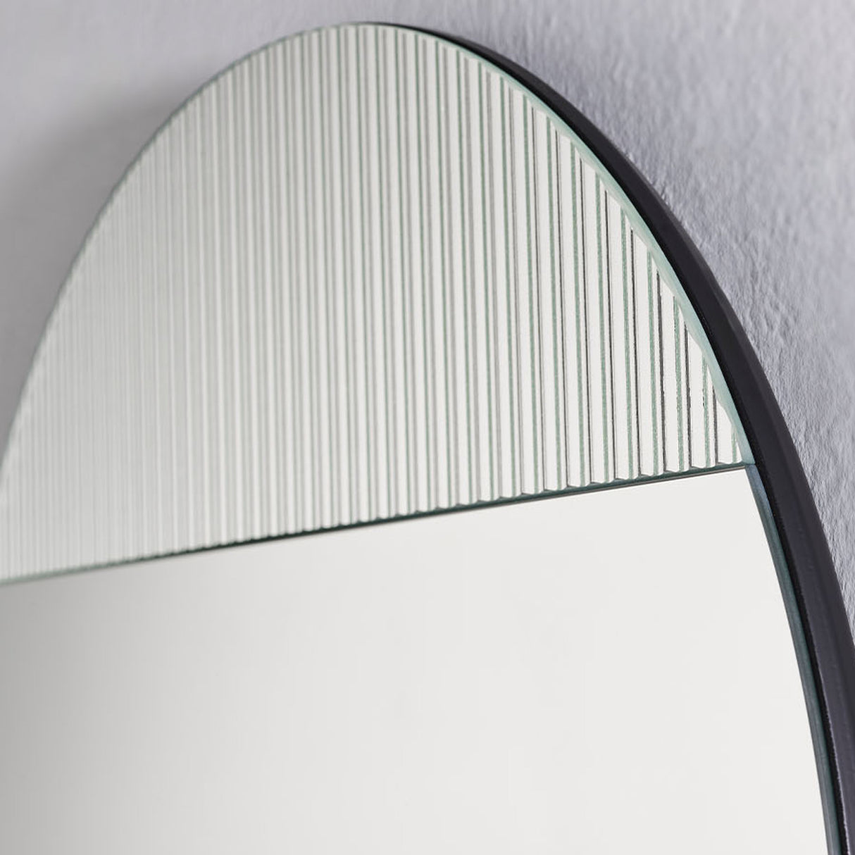 Close-up of the upper arc, the ribbed panel and the plain mirror meeting on the same frameless sheet of glass.