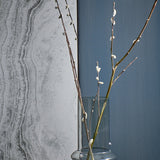 Close-up of the pale grey stone print beside a blue wall, with willow branches standing in a glass vase in front of it.