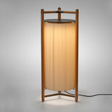 Kando P/111 Ribbon LED floor lamp with a tall pleated white cylinder shade in a wood three-legged frame and dark top disc, glowing softly against a plain grey background.