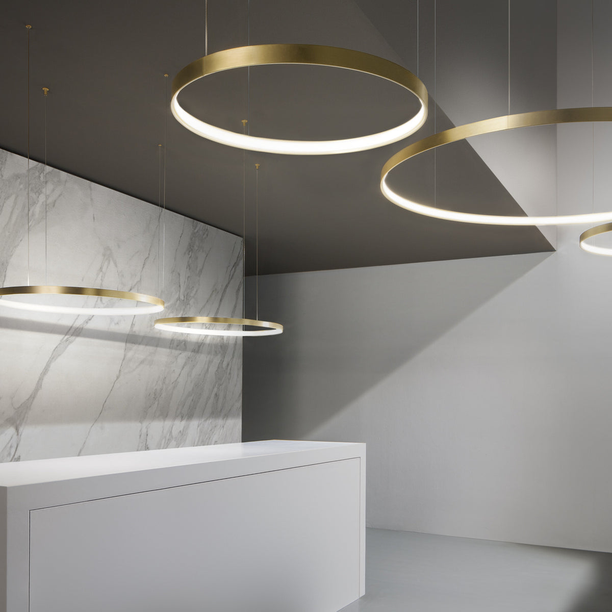 Zero Round Aluminium Ring LED Pendant Light in brushed brass, shown as multiple circular fixtures of varying sizes suspended above a marble-clad reception counter.