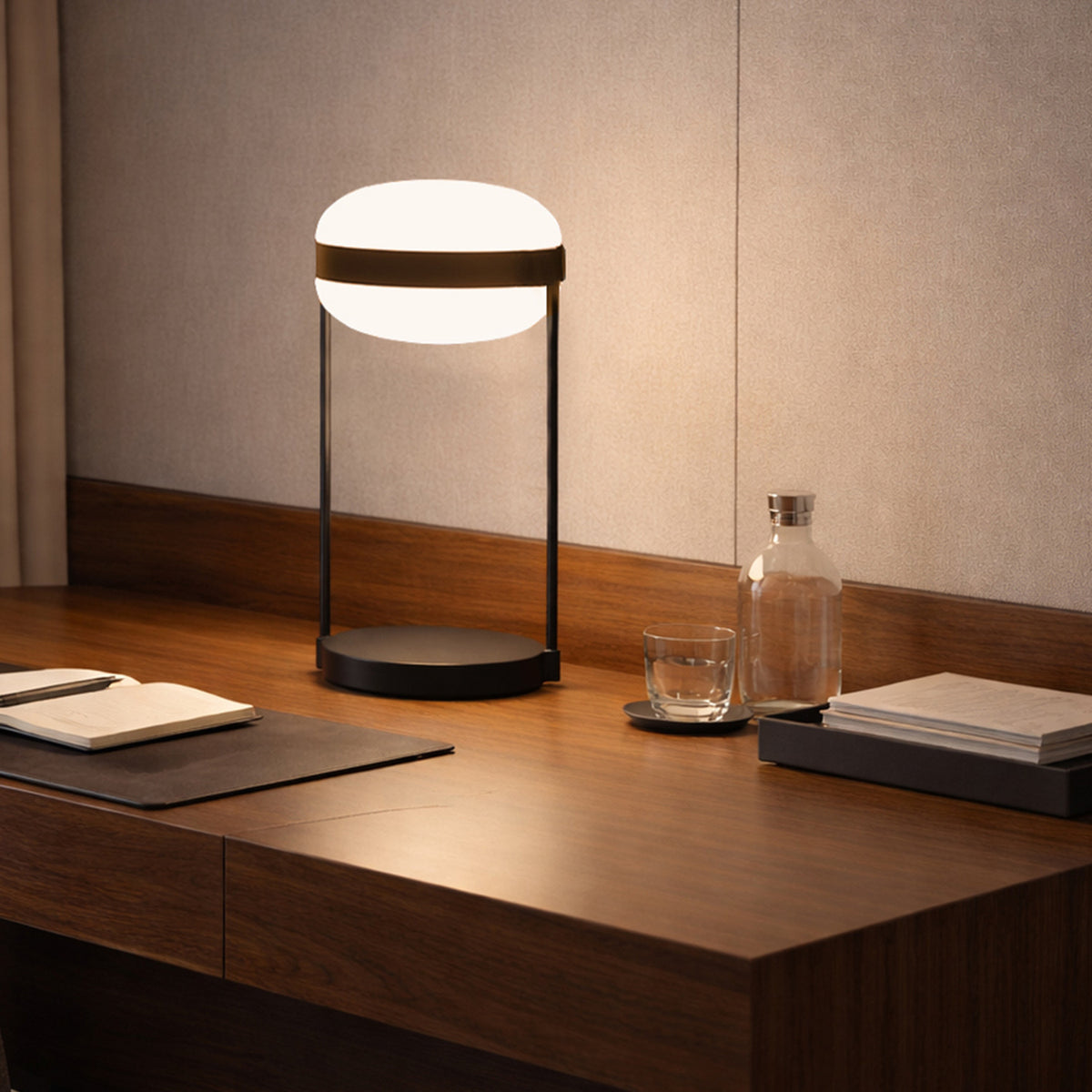 Beaded T Glass LED Table Lamp with an opal white flattened spherical shade, dark centre band and slim rods on a round black base, shown lit on a wooden desk.