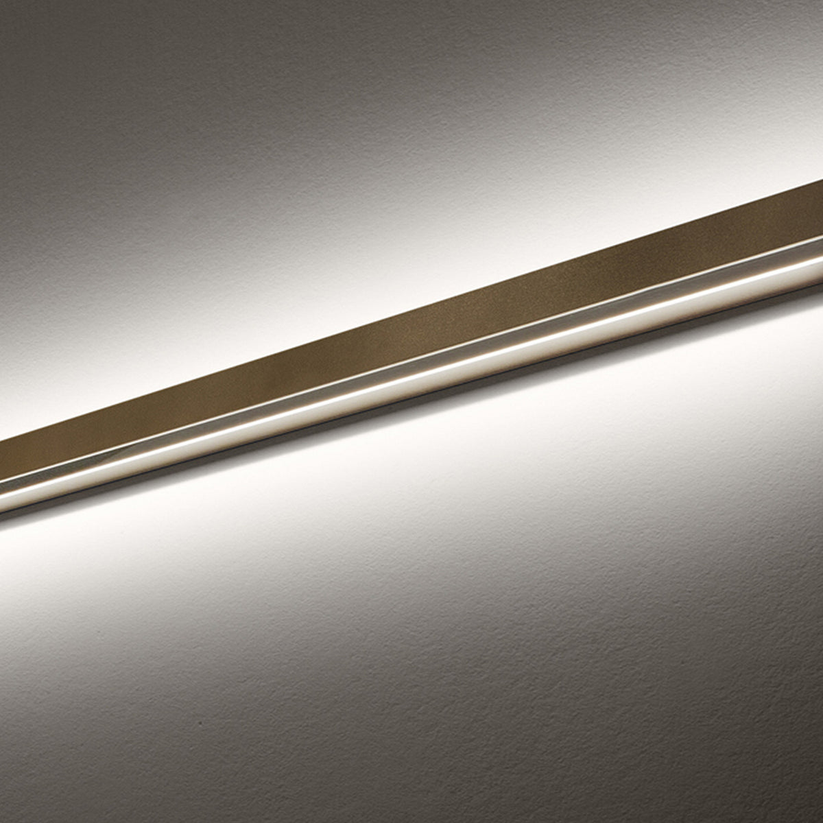 Close-up of the Zero Line Metal Linear LED Wall & Ceiling Light, a slim bronze bar with a recessed edge casting warm white light across a plain grey wall.