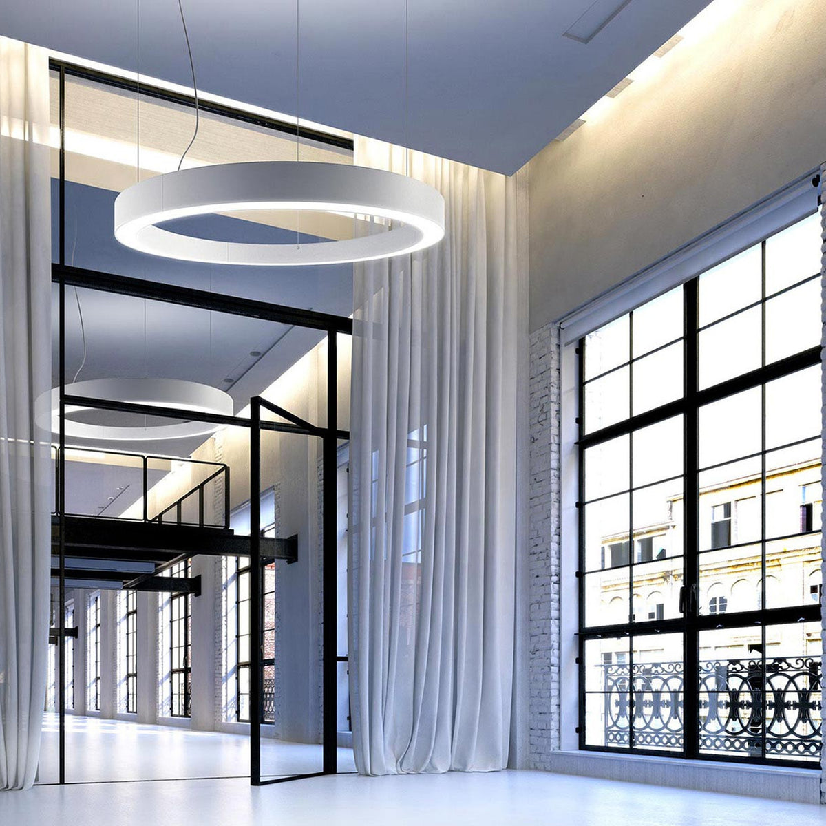 Golden Ring Aluminium LED Pendant Light in white, shown as a large circular ring fixture hanging in an open loft space with industrial windows and sheer curtains.
