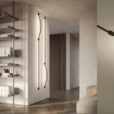 Bow Wall 300 wall light in matt black, two slim linear LED strips with gentle curves and fixing boxes, mounted on a plaster wall in a hallway setting.